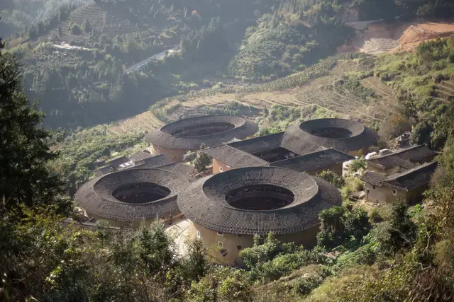 The Tianluokeng tulou cluster in Fujian: four round earthen houses and one square one among terraced green hills, seen from the hillside above