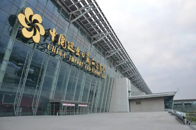 The glass facade of the Canton Fair Complex in Guangzhou, carrying the fair's golden flower emblem and the words China Import and Export Fair in Chinese and English.
