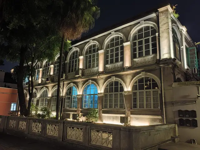 A two-storey colonial-era building with arched windows on Shamian Island in Guangzhou, floodlit at night behind a stone balustrade and trees.