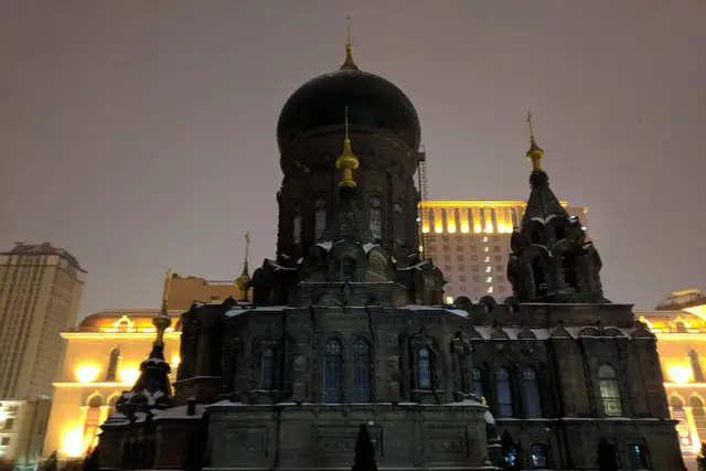 Saint Sophia Cathedral in Harbin on a January night, snow resting on its roofs and the floodlit buildings of the square glowing behind its dark dome.
