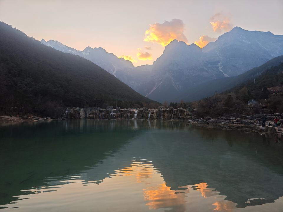 Blue Moon Valley at dusk, with the still lake reflecting sunset clouds and the peaks of Jade Dragon Snow Mountain behind.