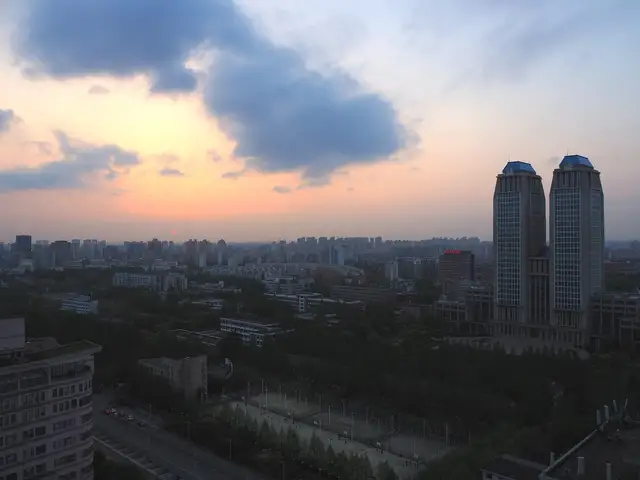 The Guanghua Twin Towers of Fudan University rise above the tree-covered Handan campus in Shanghai at sunset, seen from a high vantage point.