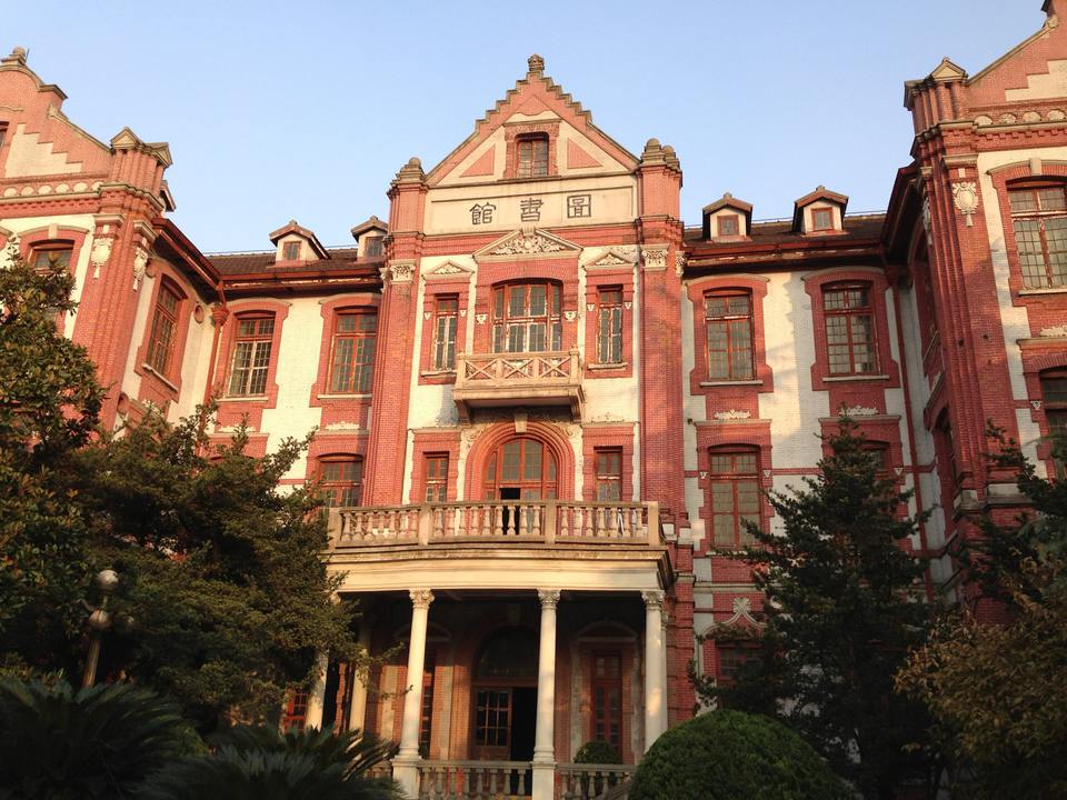 The red-brick Old Library on the Xuhui campus of Shanghai Jiao Tong University, with a columned entrance porch and gabled roofline in warm afternoon light.