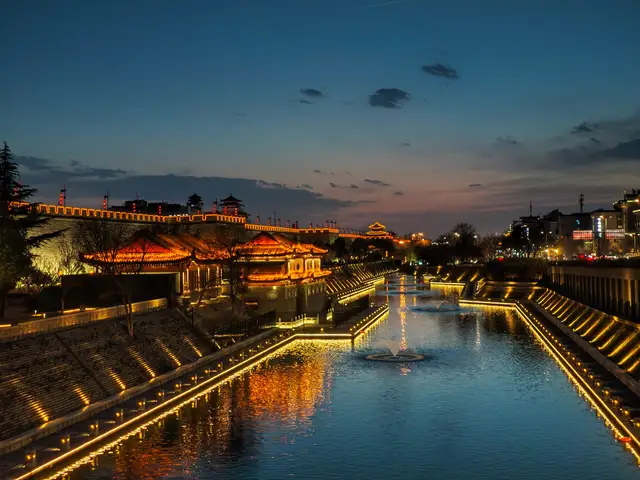 The Xi'an city wall outlined in lights at dusk, with pavilions and the moat in the foreground.